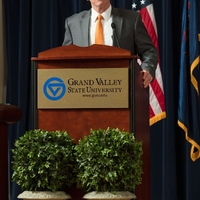 Doctor Potteiger standing at a GVSU poidum on stage, holding onto the sides as he speaks